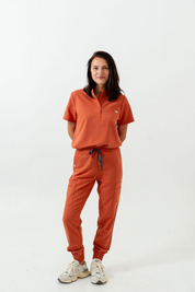 A person standing wearing orange scrub pants and a matching top with a collar, with 8 pockets on the pants.