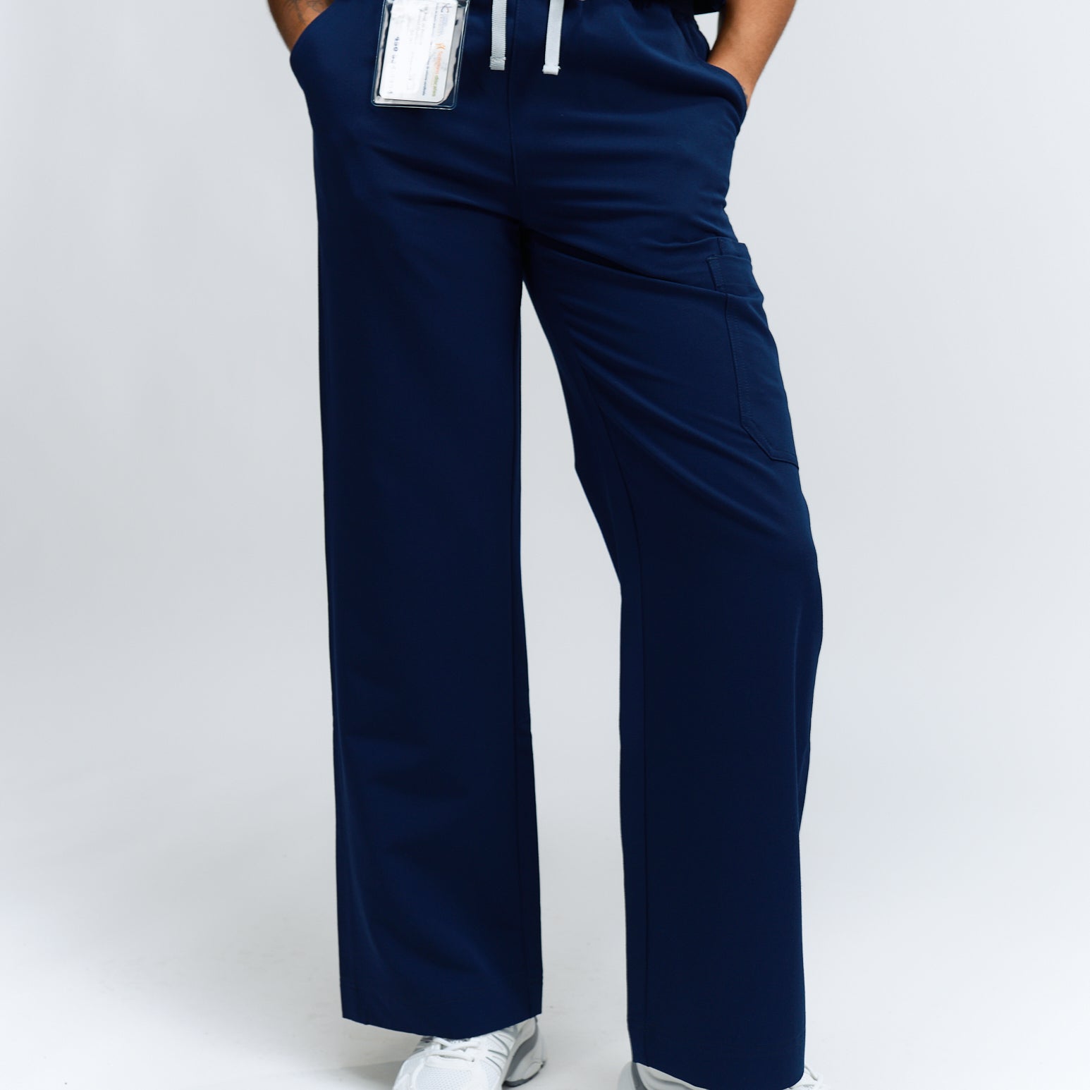 A person wearing navy wide leg scrub pants with an elastic waistband, standing against a white background.