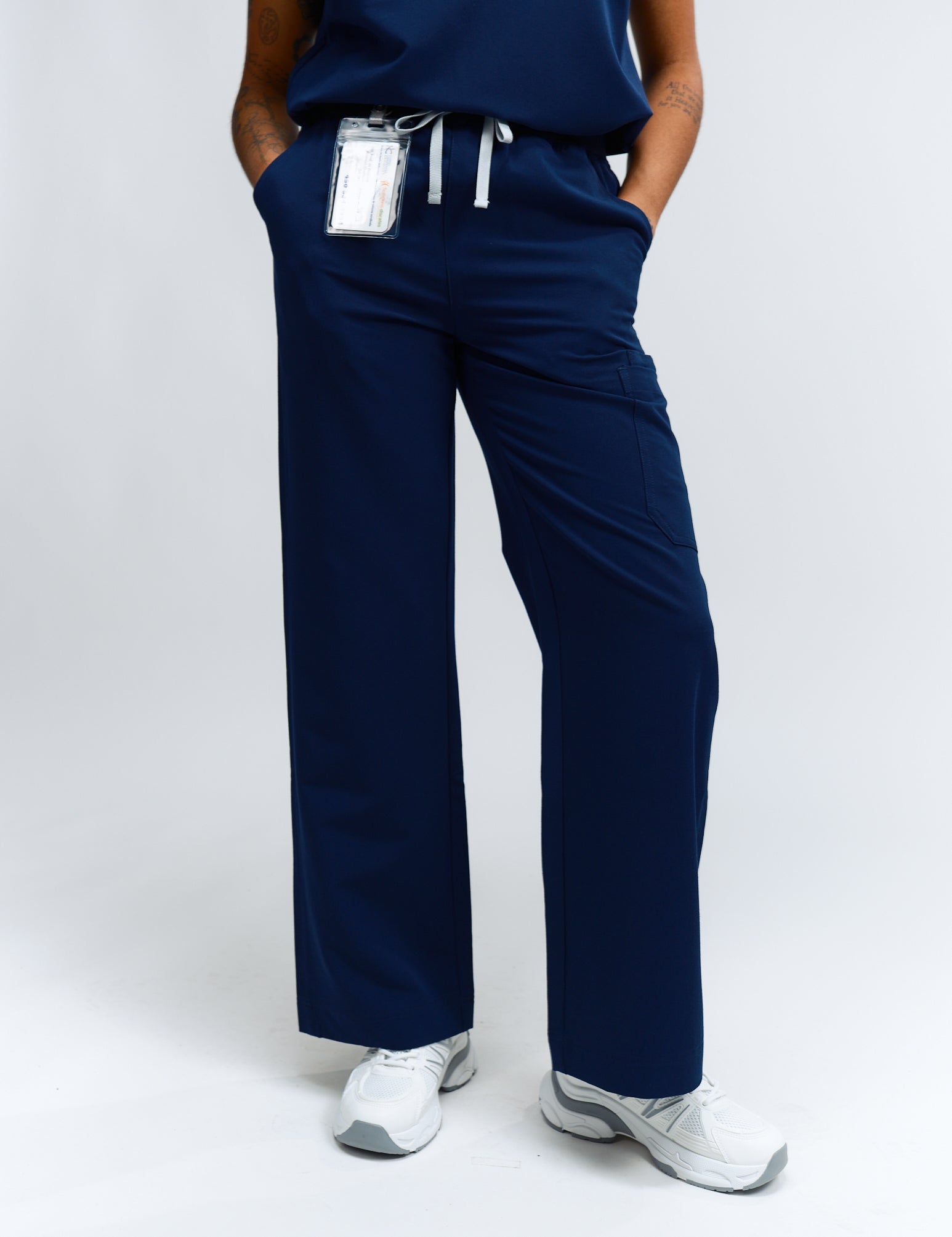 A person wearing navy wide leg scrub pants with an elastic waistband, standing against a white background.