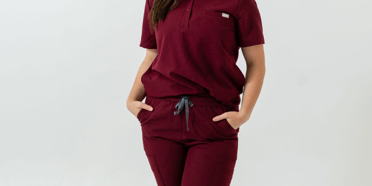 A person standing wearing burgundy scrub pants with multiple pockets and a drawstring waist.