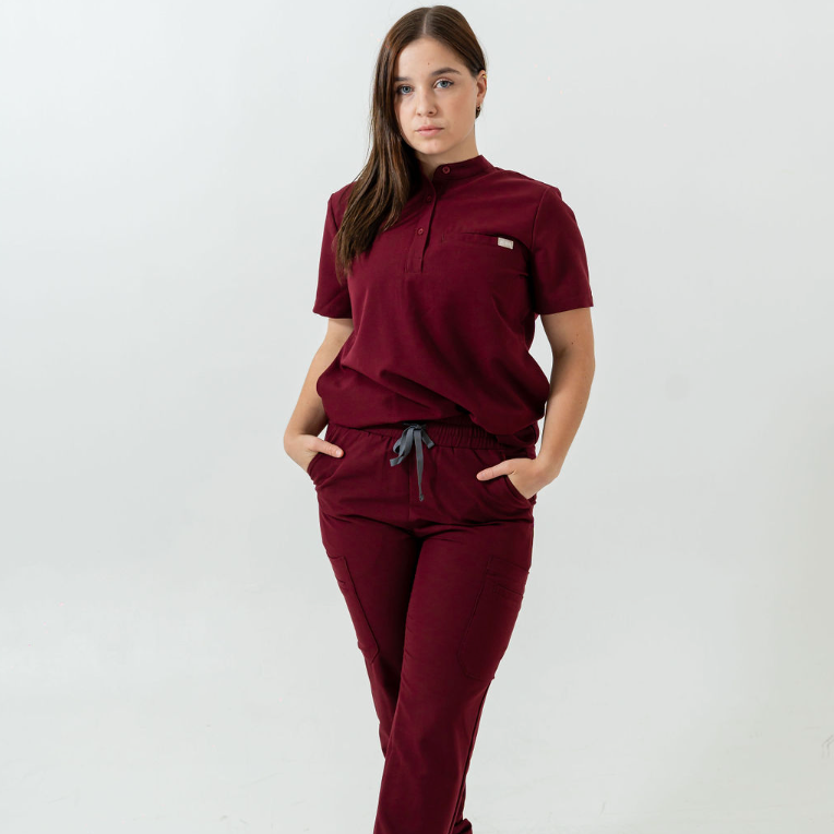 A person standing wearing burgundy scrub pants with multiple pockets and a drawstring waist.