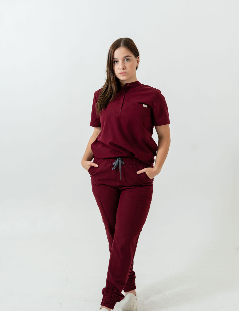 A person standing wearing burgundy scrub pants with multiple pockets and a drawstring waist.