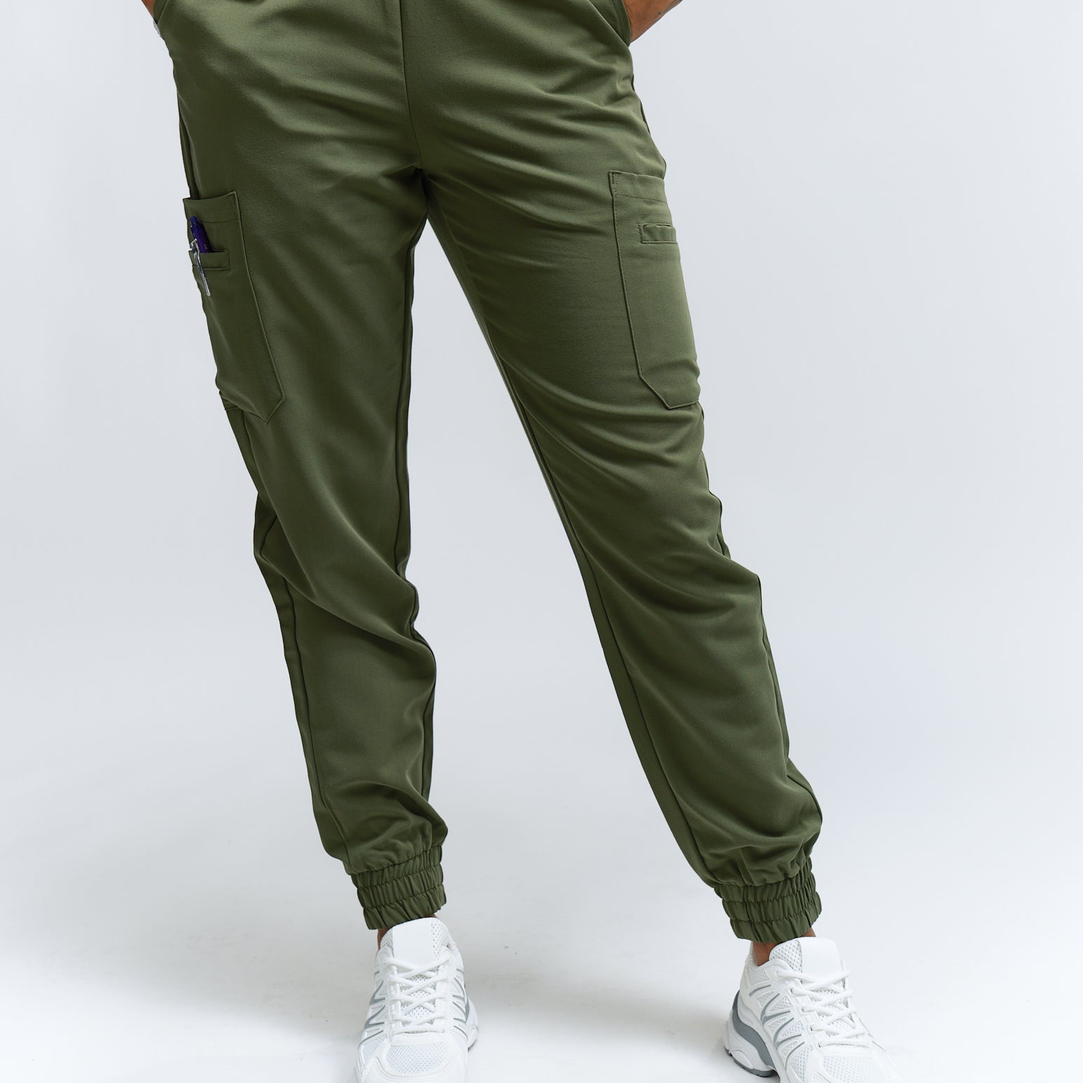 A person wearing mossy green scrub pants with multiple pockets and a drawstring waist, paired with white sneakers.