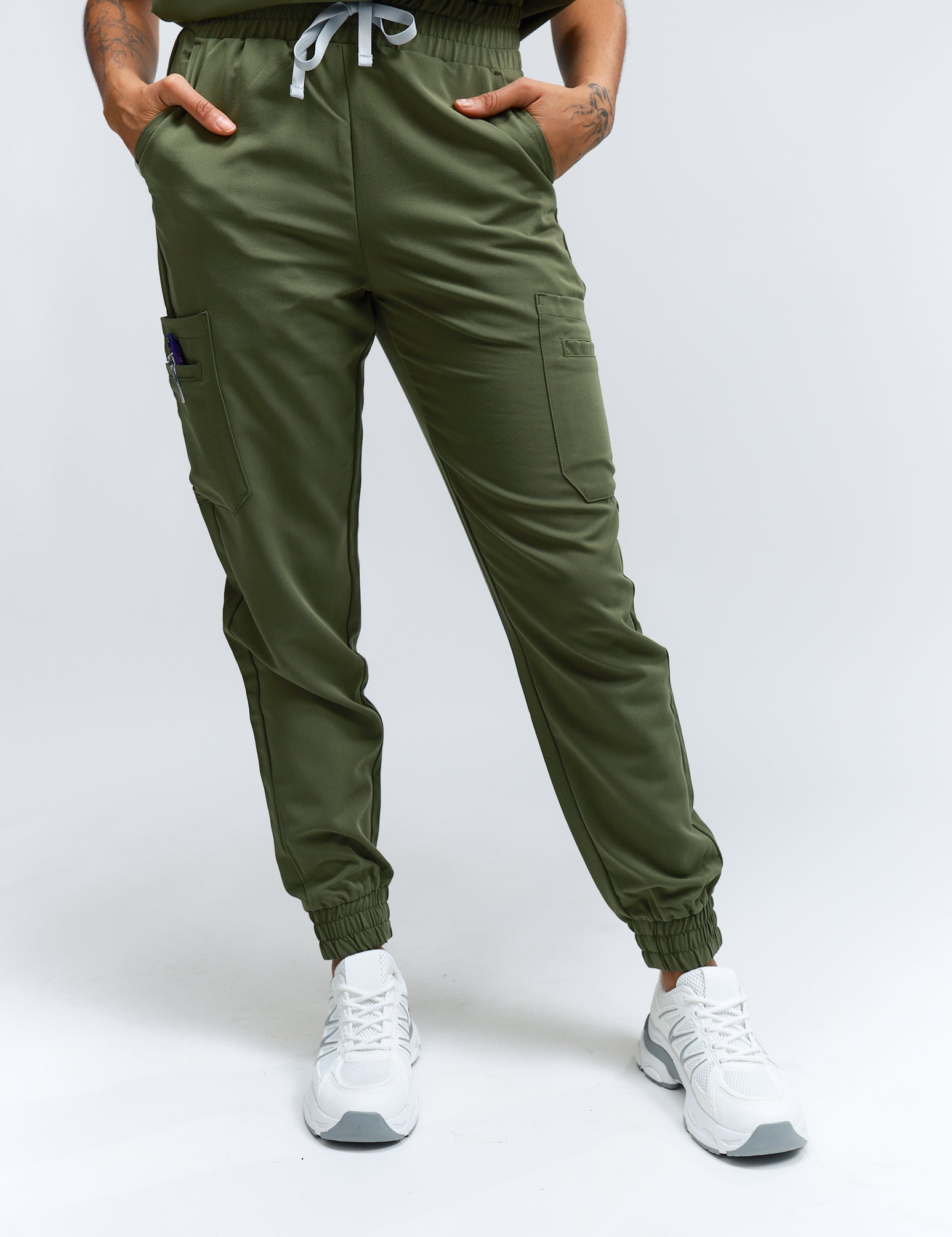A person wearing mossy green scrub pants with multiple pockets and a drawstring waist, paired with white sneakers.