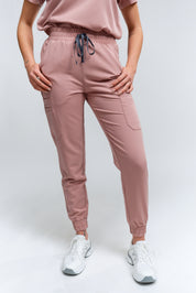 Un pantalon de jogging couleur bois de rose avec de multiples poches et un cordon de serrage à la taille, associé à des baskets blanches.